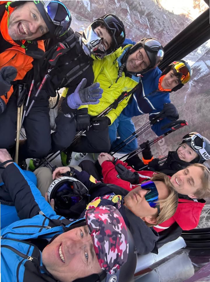 Selfie de huit skieurs serrés dans une télécabine, casques et masques sur la tête, tout sourire